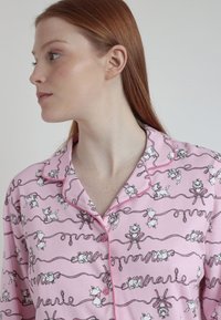 Camisón rosa con cuello, que presenta un patrón de gatos y lazos, con contornos negros y acentos rosas, hecho de tela suave.