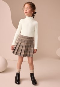 Col roulé blanc à côtes associé à une jupe plissée à carreaux marron, des bottines noires et des chaussettes en tricot beige clair.