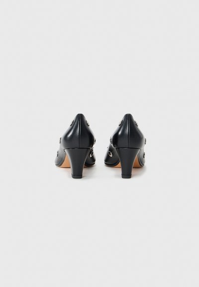 Black leather high-heeled shoes with a pointed toe, featuring circular silver accents on the side and a textured finish.