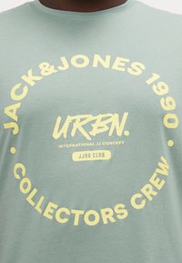 T-shirt in cotone verde chiaro con grafica circolare e testo giallo: "JACK & JONES 1990 URBN. COLLECTORS CREW JJ90 CLUB."