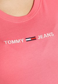 Camiseta de algodón rosa con cuello redondo y bordado de texto "TOMMY JEANS" junto con un pequeño logo de bandera en rojo, blanco y azul.