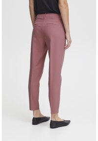 Pink tailored trousers with a smooth texture, featuring back pockets and a tapered leg design. Worn with black flat shoes.