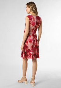 Ärmelloses Kleid mit Blumenmuster in Rosa- und Rottönen, mit eng anliegendem Oberteil und ausgestellt Rock. Kombiniert mit hellen Riemchen-Heels.