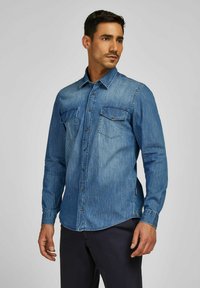 Denimhemd in Mittelblau. Lange Ärmel, spitzer Kragen, zwei Brusttaschen mit Knopfverschlüssen und gerader Saum. Glatte Textur.