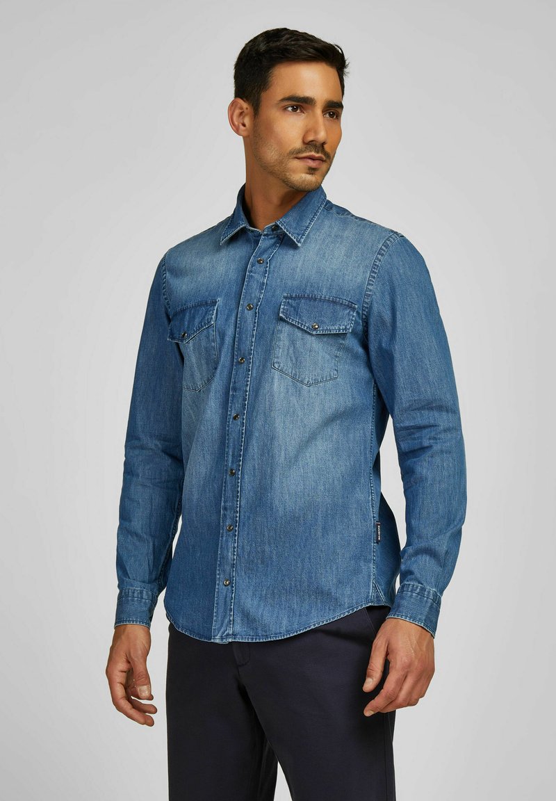 Denimhemd in Mittelblau. Lange Ärmel, spitzer Kragen, zwei Brusttaschen mit Knopfverschlüssen und gerader Saum. Glatte Textur.