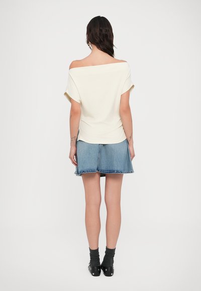 Εκρού μπλουζάκι με ανοιχτούς ώμους και κοντά μανίκια, συνδυασμένο με τζιν φούστα σε γραμμή Α με ξεφτισμένη φάσα.