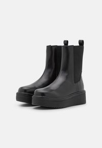 Bottines Chelsea noires avec une finition brillante, dotées de panneaux latéraux élastiques et d'un motif en crocodile texturé à l'arrière, avec une semelle épaisse.