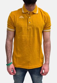 Polo shirt in cotone giallo con tre bottoni, strisce bianche a contrasto su colletto e maniche, con un piccolo logo sul petto.