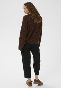 Pulover tricotat maro cu un model în diamant, asortat cu pantaloni negri taperi și pantofi maro cu șireturi. Vedere din spate.