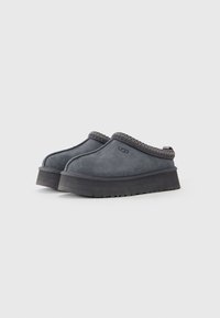 Tamno sivi slip-on cipele s debelim crnim potplatima i tkanim rubovima, s baršunastom teksturom i UGG logotipom sa strane.