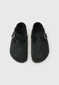 Juodi korduroviniai šlepetės su tekstūruotu paviršiumi, minkštu juodu vidumi, dviem reguliuojamomis juostelėmis ir sidabriniais sagties akcentais.