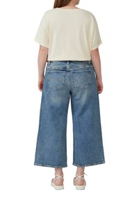 Hellbeige Oversized-T-Shirt, kombiniert mit weit geschnittenen Jeans im mittleren Waschton. Die Jeans haben zwei hintere Taschen und einen fransigen Saum.