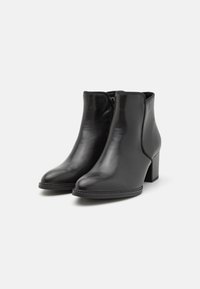 Bottines en cuir noir avec un bout arrondi, fermeture éclair et un talon épais. Texture lisse et design minimaliste.