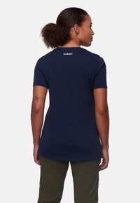 Mørkeblå t-shirt lavet af blødt stof, med korte ærmer og en lidt længere bagdel. "MAMMUT" logo i hvid på den øverste del af ryggen.