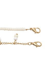 Złote klipsy metalowe łączą dwa łańcuchy. Górny łańcuch ozdobiony jest małymi białymi koralikami; dolny ma większe białe koraliki z teksturowanym ogniwem.