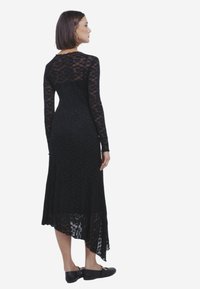 Zwarte kanten jurk met lange mouwen, met een high-low zoom en bloemenpatroon. Gladde textuur, nauwsluitend silhouet en subtiele details.