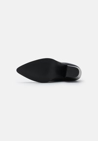 Zapato de tacón alto negro con puntera afilada y suela texturizada, con un material superior liso y un diseño de tacón en forma de cono.