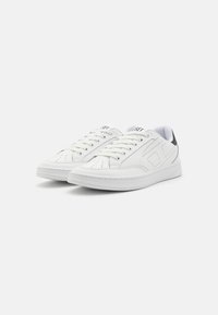 Vita lädersneakers med rund tå, vadderad tunga och en svart hälaccent. Har perforeringar för andningsförmåga och platta snören.