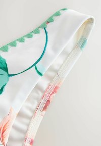 Top de bikini floral cu material alb, având accente brodate verzi de-a lungul marginii și o textură netedă, elastică.