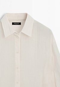 Chemise blanche boutonnée avec col pointu et fines rayures verticales texturées, étiquette Massimo Dutti.