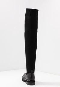 Botas negras sobre la rodilla con un upper texturizado de punto y una plantilla de cuero suave, que cuentan con una suela plana y un diseño acanalado en el tobillo.