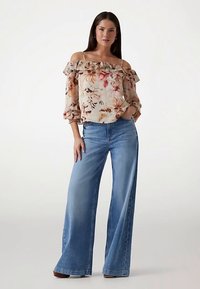Blouse fleurie à épaules dénudées en tissu léger, dotée de manches volantées ; associée à un jean bleu délavé à jambes larges ; coupe décontractée.