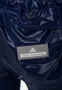 Marina blå atletiska shorts tillverkade av glänsande, lätt material, med en grå etikett med "adidas" och "stella mccartney" varumärke.