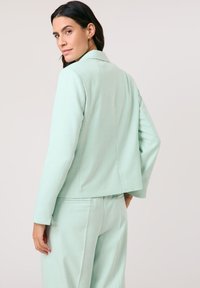 Mintgrüner Blazer mit Reverskragen und langen Ärmeln, ausgestattet mit einem leicht lässigen Schnitt und strukturiertem Stoff. Kombiniert mit passenden Hosen.