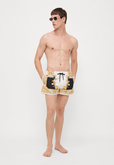 Maillots de bain avec un design noir et blanc, ornés de motifs floraux dorés et d'une taille à cordon. Fabriqués en tissu léger avec des poches.