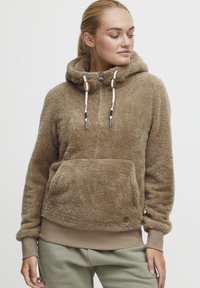 Pahuljasti smeđi dukserica s polu-zip zatvaranjem, prilagodljivom kapuljačom i prednjim kengur džepom; ima rebraste manžete i mekan, teksturiran finiš.