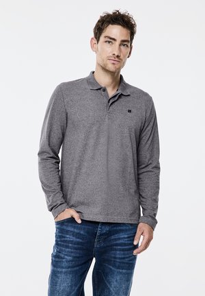 Graues Langarm-Polohemd mit einer strukturierten Oberfläche und einem knöpfbaren Kragen. Ein kleines Logo befindet sich auf der linken Brust. Kombiniert mit blauen Jeans.