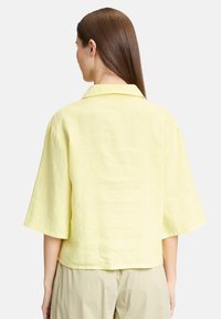 Camicia a maniche corte con colletto in lino giallo chiaro, dalla vestibilità rilassata, caratterizzata da una texture liscia e un orlo che si trova sopra la vita.