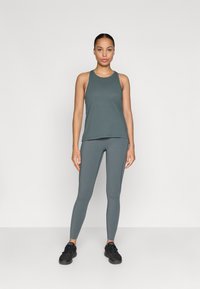 Pelēks sporta topiņš un atbilstošas legingu bikses, izgatavotas no elastīga auduma. Apģērbs ir brīvs un ar gludu tekstūru, bez redzamām rakstu apdruku.