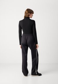 Haut noir à manches longues associé à un pantalon de sport sombre, texturé, avec taille élastiquée, présentant des rayures blanches sur les côtés et des chaussures noires.