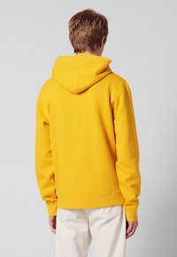 Sweat-shirt à capuche jaune avec une coupe décontractée, fabriqué en matériau doux. Comprend une poche kangourou et des détails de poignets côtelés.