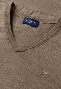 Khaki v-hals trui gemaakt van zachte stof. Bevat een subtiel geborduurd logo op de borst en heeft een gladde, gelijkmatige textuur met zichtbare stiknaden.