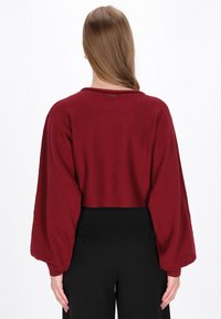 Bordeaux kort gebreid sweater met ballonmouwen, geribbelde manchetten en een eenvoudige halslijn, gecombineerd met zwarte high-waisted broeken.