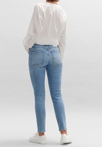 Tajta blå jeans med medelhög midja och två bakfickor, kombinerat med en långärmad vit topp och vita sneakers.