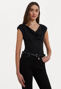 Melnas cowl-neck bodysuit ar kroku plecu detaļām, saskaņota ar melnām augsto jostasvietu džinsiem un šauru melnu jostasvietu ar sudraba sprādzi.