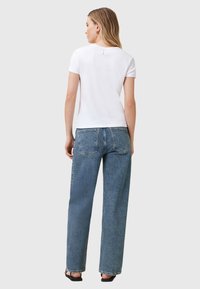 T-shirt bianco a maniche corte con scollatura rotonda, abbinato a jeans a vita alta di colore blu chiaro con gamba dritta e dettagli di cucitura delicati.