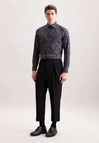 Camicia scura a maniche lunghe con un motivo paisley multicolore, abbinata a pantaloni neri a vita alta e scarpe nere stringate.