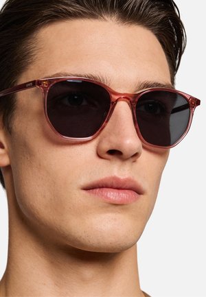 Occhiali da sole con lenti scure e una sfumatura rosa, dal design classico. Realizzati in plastica trasparente con una texture liscia, con un marchio discreto sulla stanghetta.