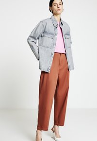 Giacca di jeans azzurro con due tasche sul petto, abbinata a una t-shirt rosa e pantaloni a gamba larga color ruggine. Mules bianchi con tacco.