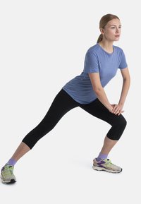 Camiseta deportiva azul claro de manga corta, combinada con leggings capri negros y zapatillas de correr multicolores con detalles verdes y calcetines morados.