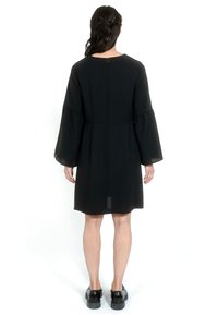 Crna haljina s dugim, lepršavim rukavima i ravnim siluetom. Ima blagi sjaj i zatvaranje na patentni zatvarač na leđima. Ravna obuća.