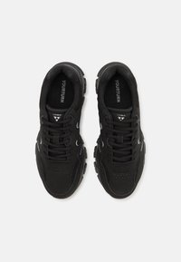 Chaussures de sport noires dotées d'une tige en mesh, d'un col rembourré et d'une semelle extérieure en caoutchouc texturée. Les lacets et le texte du logo sont des détails marquants.