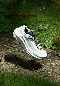 Light green running shoe with mesh upper, black accents, textured sole, and lacing system, set against a natural grassy background.