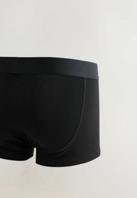 Boxer noirs pour homme avec une large ceinture élastique et des coutures visibles sur un fond clair uni.