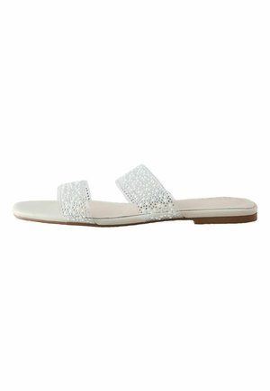 Weißer flacher Slide-Sandal mit zwei perlenbesetzten Riemen und einer beigen Sohle mit dünner brauner Laufsohle.