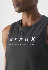Top atletico senza maniche di colore nero con il logo "HYROX" in testo bianco. Il tessuto sembra liscio, con scollatura rotonda e vestibilità atletica.